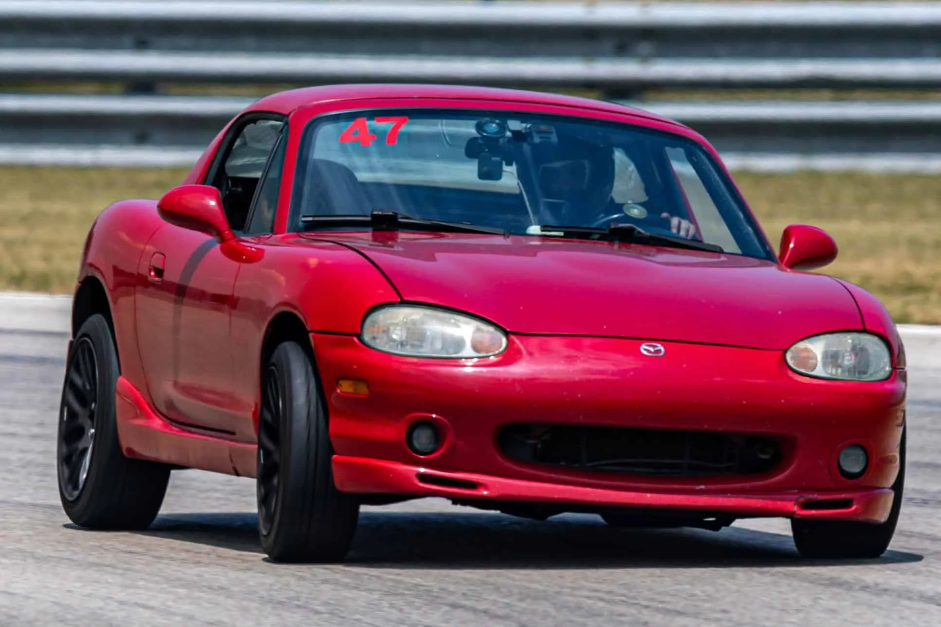 Red NB Mazda Miata with number 47 on the windshield, cornering toward the camera on track