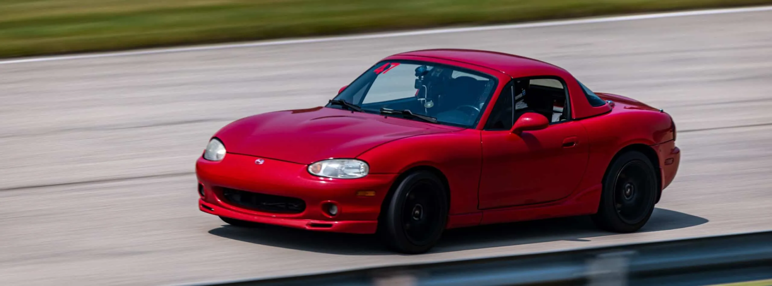 Red NB Mazda Miata with a hardtop and number 47 on the windshield, panning shot at speed on track