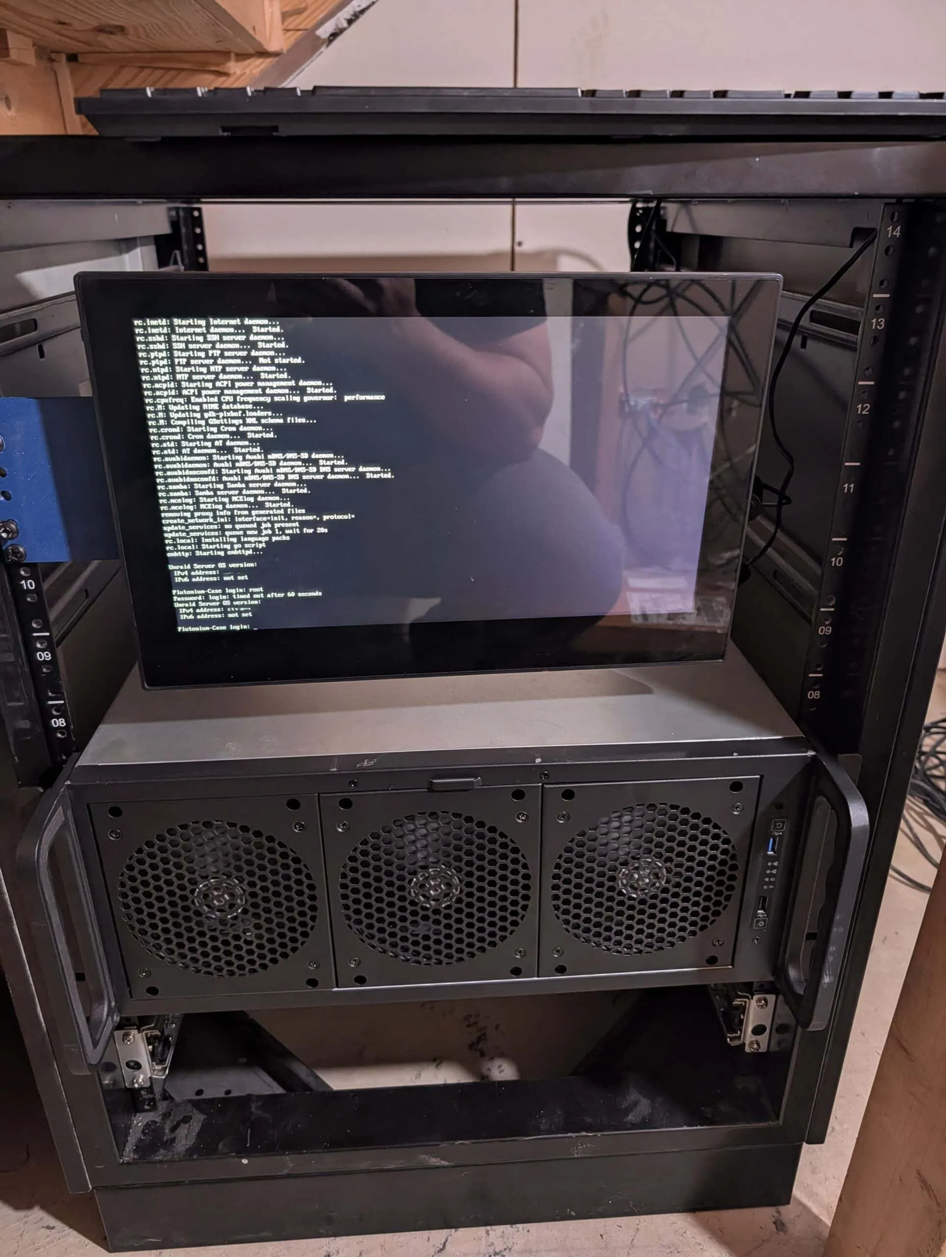 Network rack with a 3D printed bracket holding a monitor showing Unraid boot output above the new 4U server with three front fans